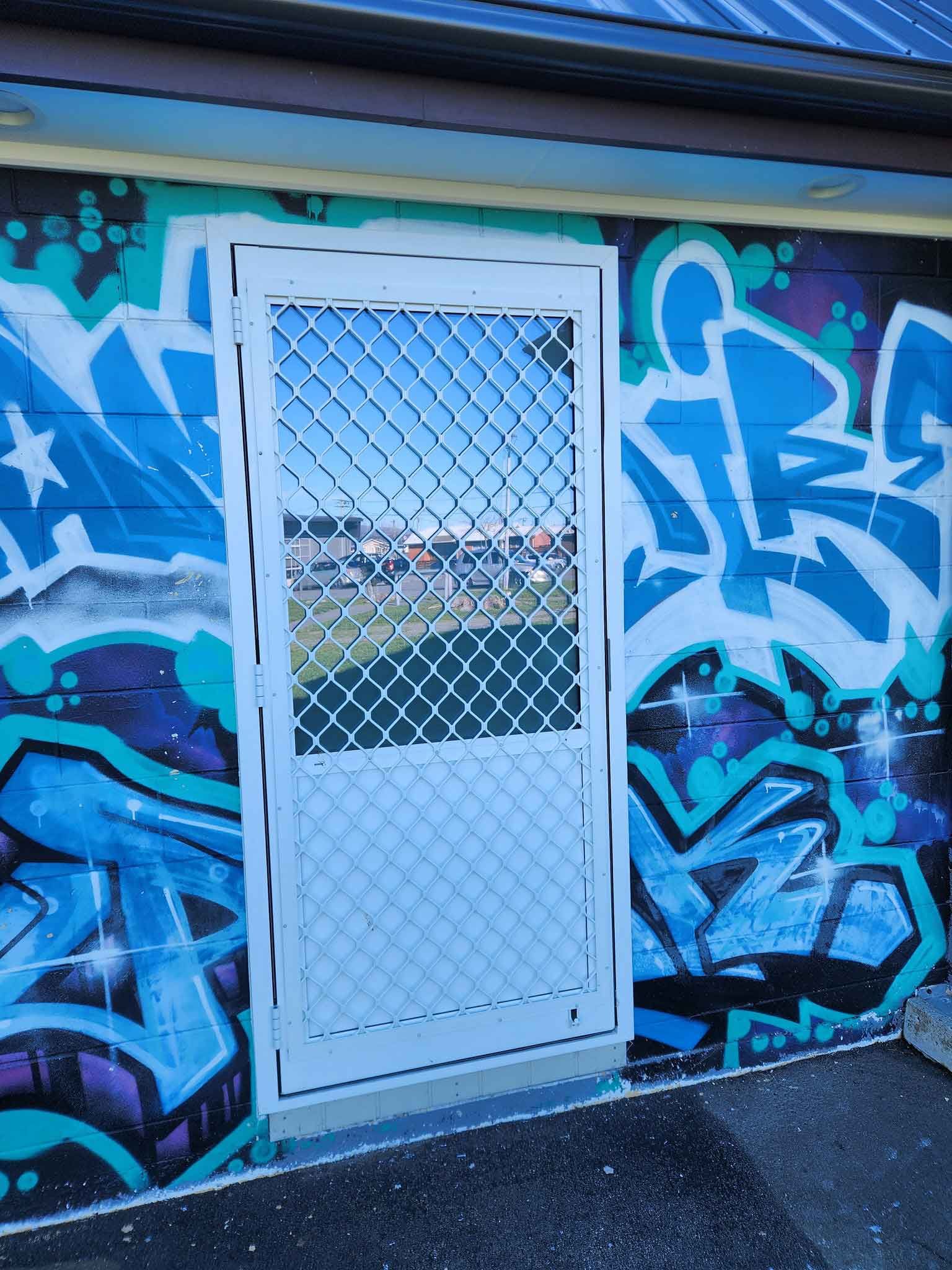 A white door is sitting in front of a wall with graffiti on it.