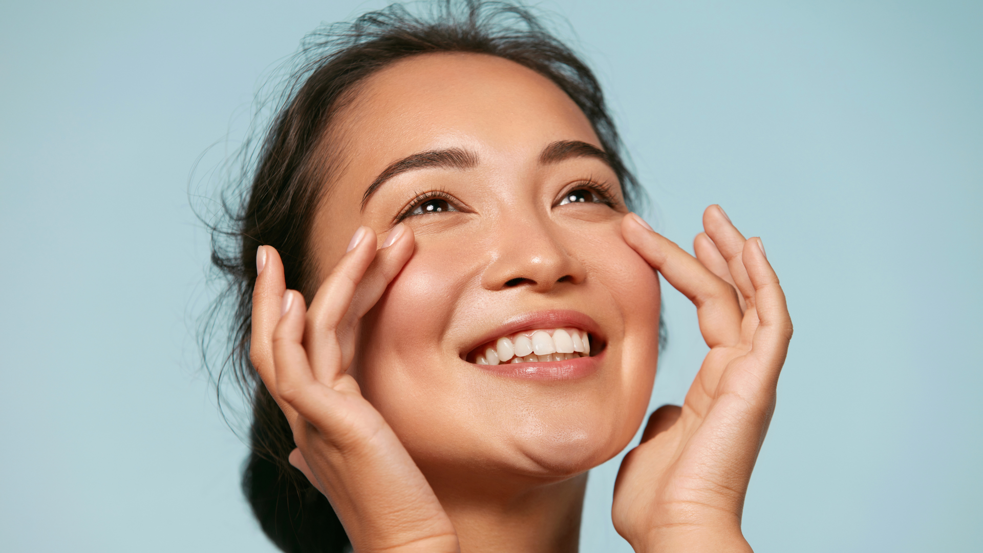 Smiling person touching their face against a light blue background
