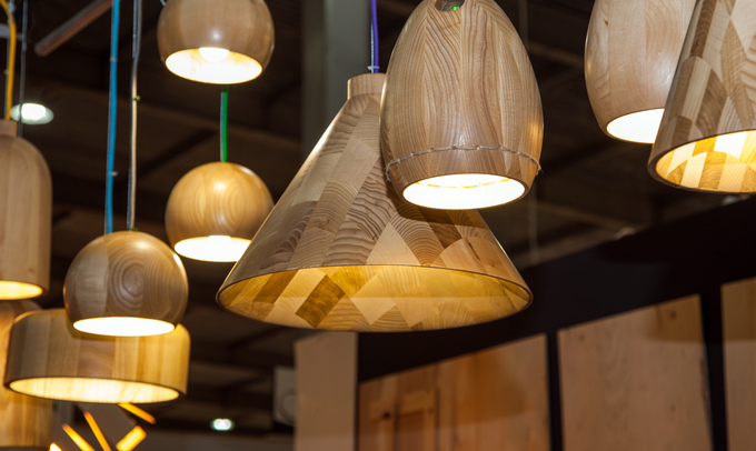 Wooden pendant lights of various shapes hanging from the ceiling, illuminated, in a showroom setting.
