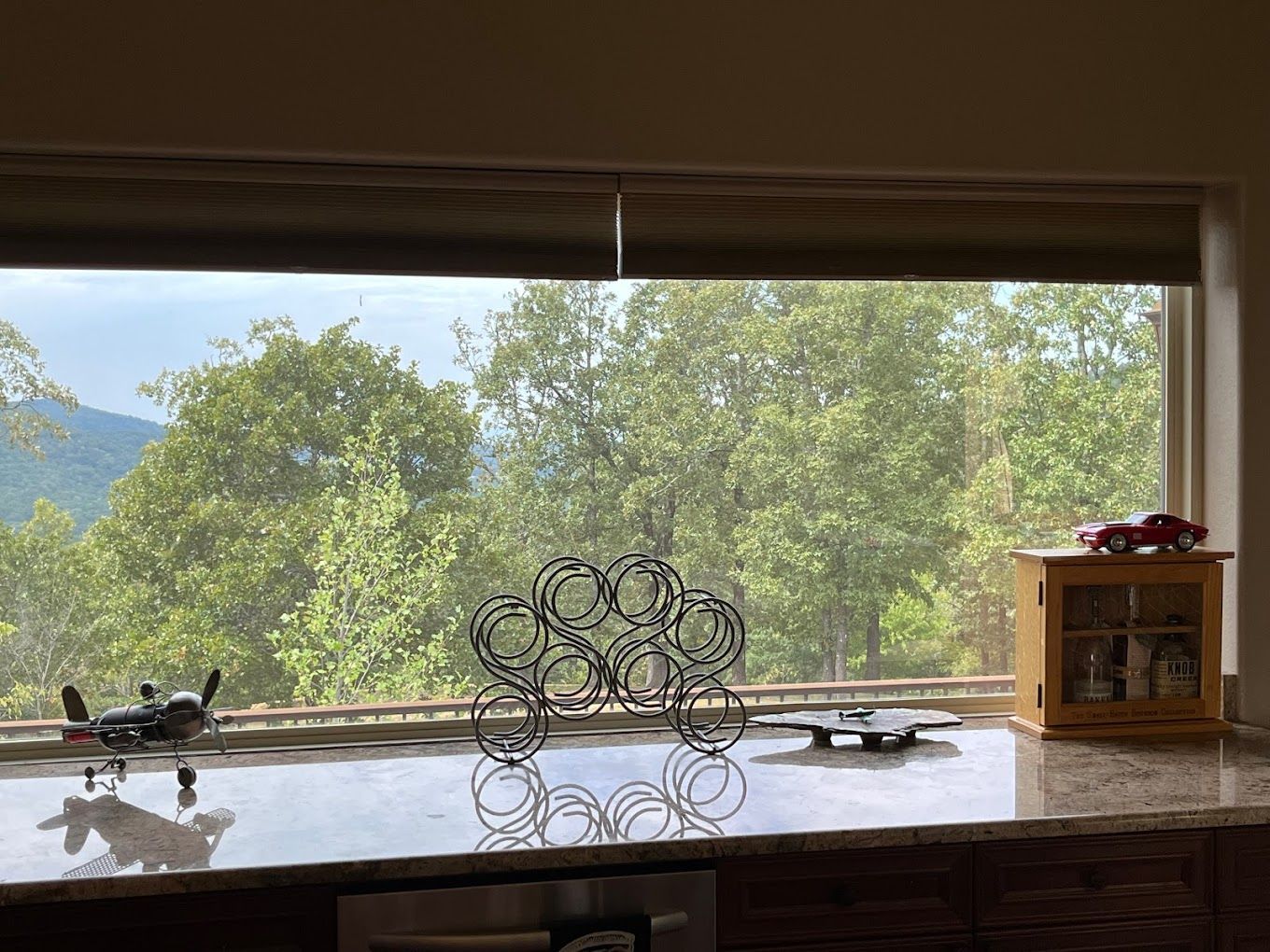 A kitchen counter with a view of trees and mountains through a window.