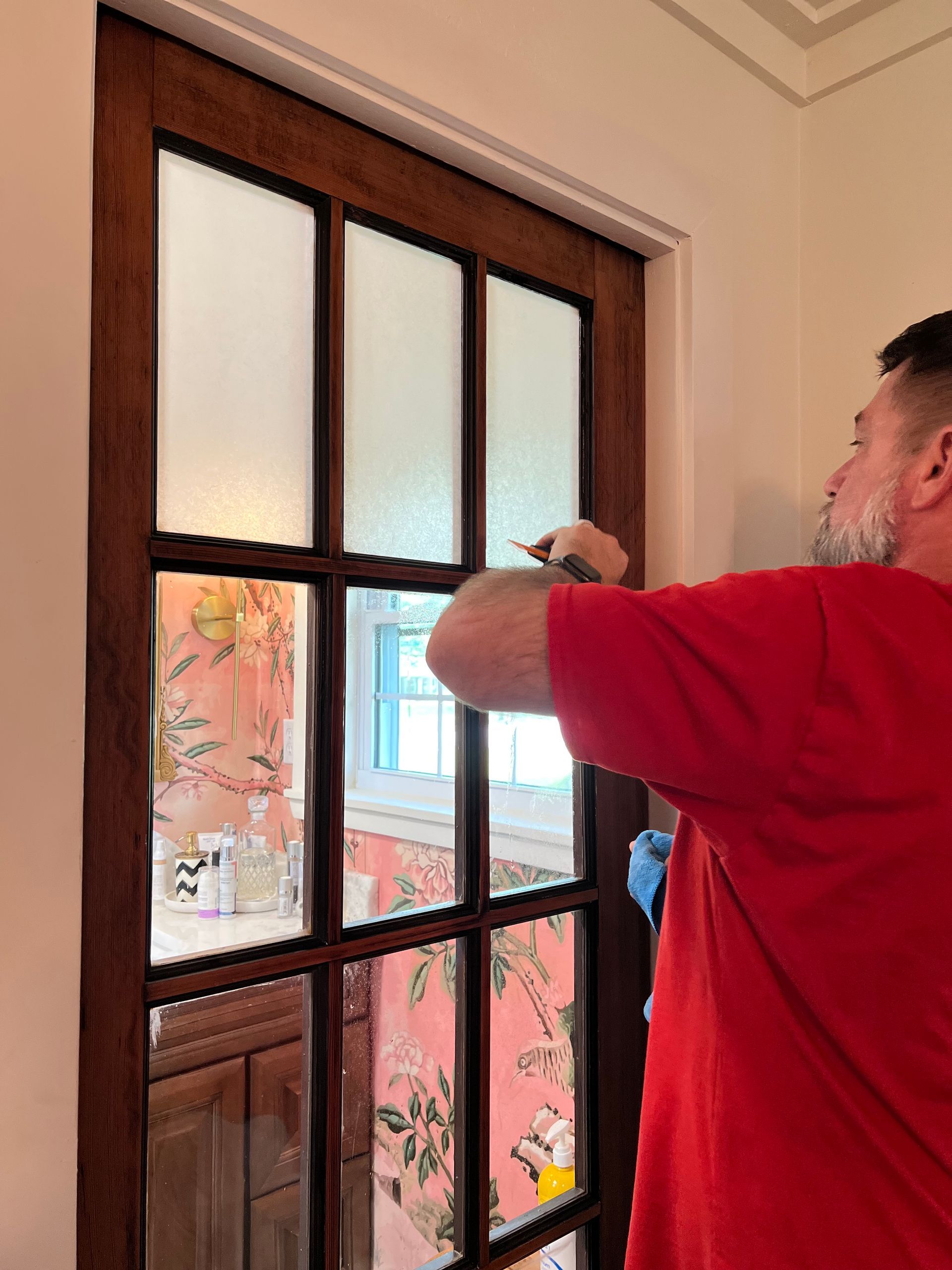 A man in a red shirt is cleaning a window with a brush.