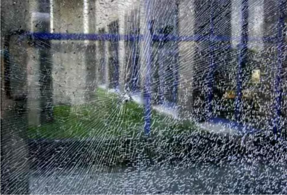 A sprinkler is spraying water on a broken glass window.