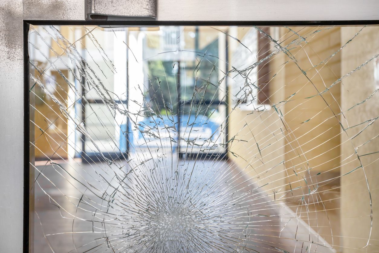 A broken glass door with a reflection of a building in it.