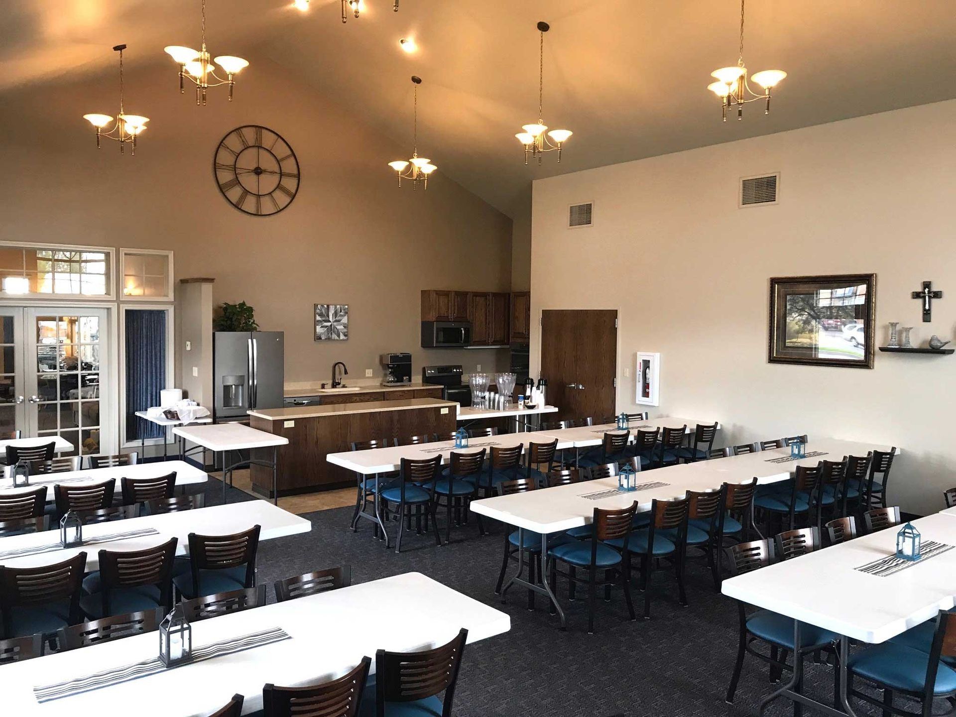 Large room with tables set for a gathering, kitchen area, and a large clock on the wall.