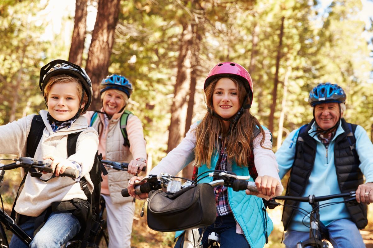 Family biking in a forest; smiling, wearing helmets, sunny day.