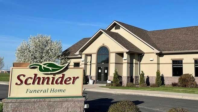 Sign for Schnider Funeral Home in front of a tan building under a blue sky.