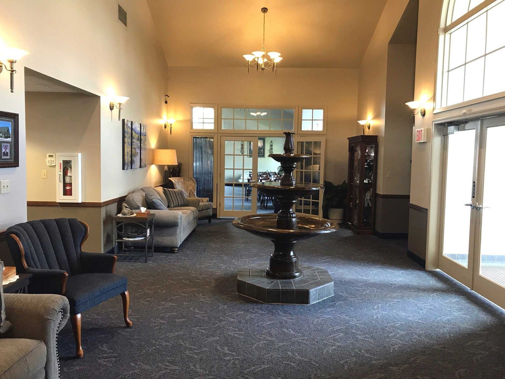 Lobby with fountain, seating, and entry doors. Beige walls, carpeted floor, and decorative lighting.