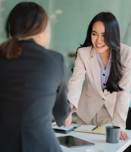 A woman is shaking hands with another woman while sitting at a table.