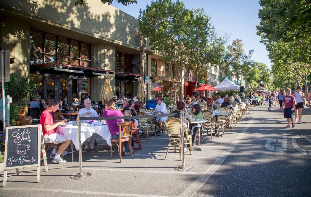 A group of people are sitting at tables outside of a restaurant.