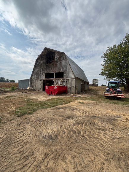 Old weathered barn with red dumpster in the entrance and tractor nearby on a cloudy day.