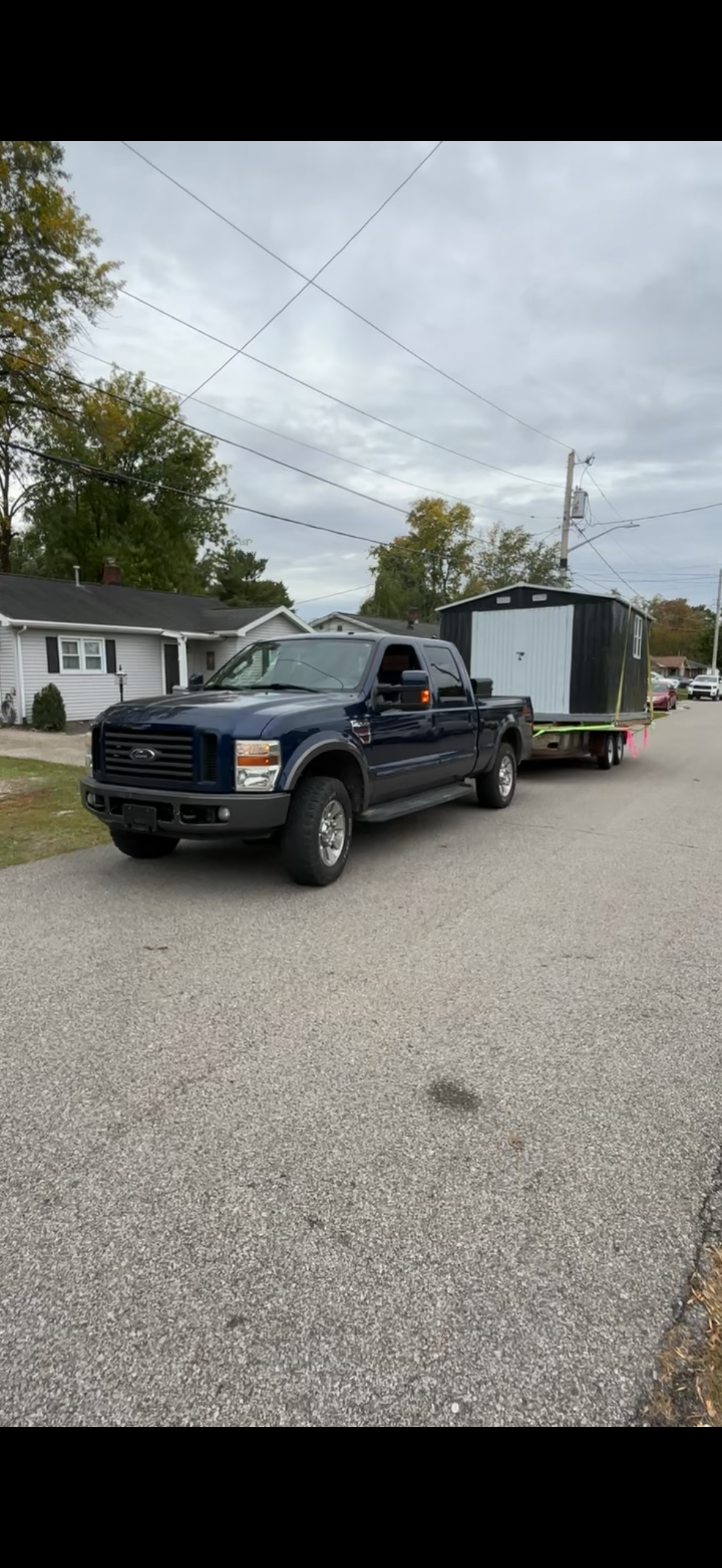 A blue pickup truck towing a white enclosed trailer on a paved road in front of houses.