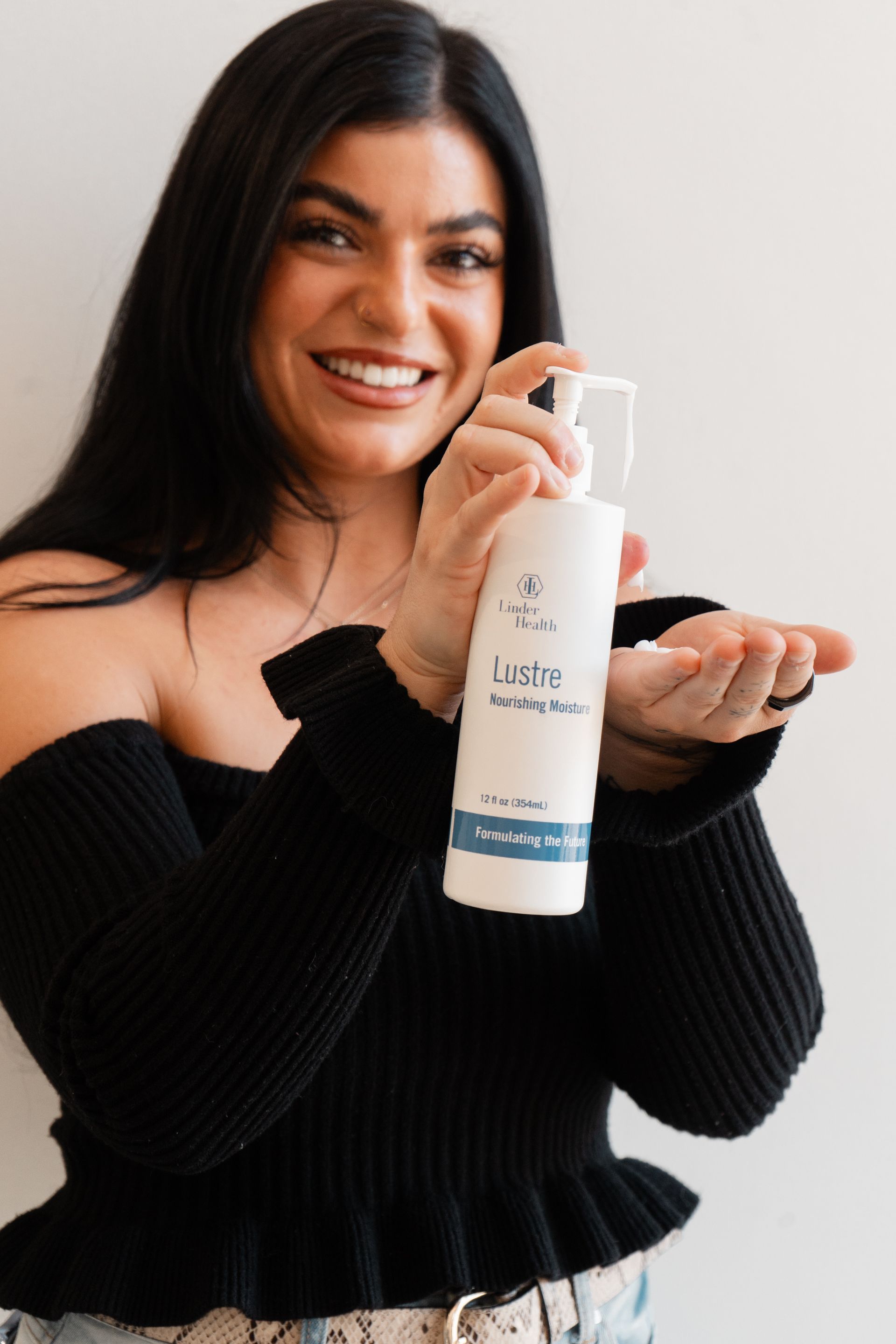 Smiling woman holding a white bottle of lotion and rubbing cream on her hand
