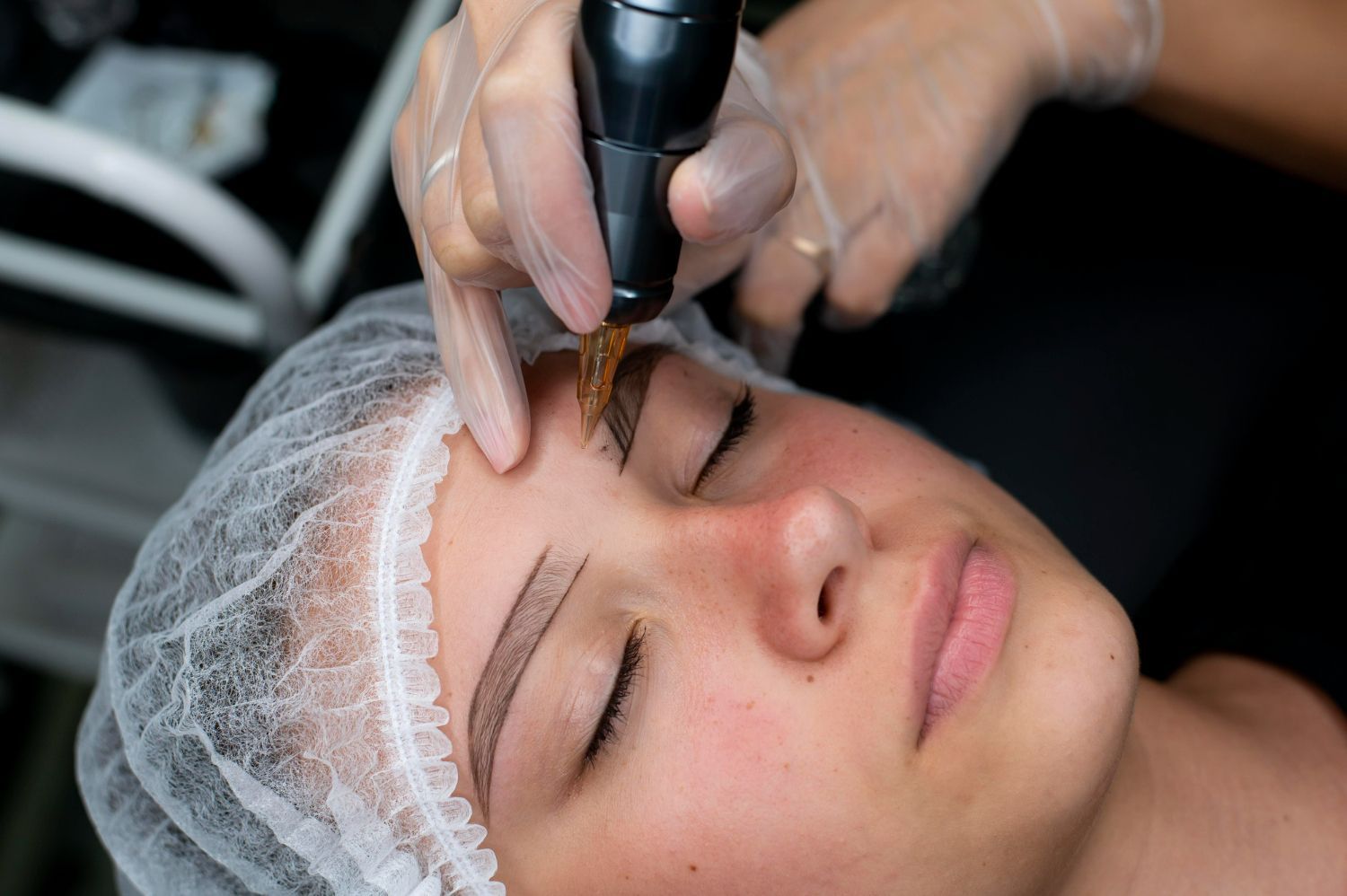 A woman is getting her eyebrows tattooed with a machine.