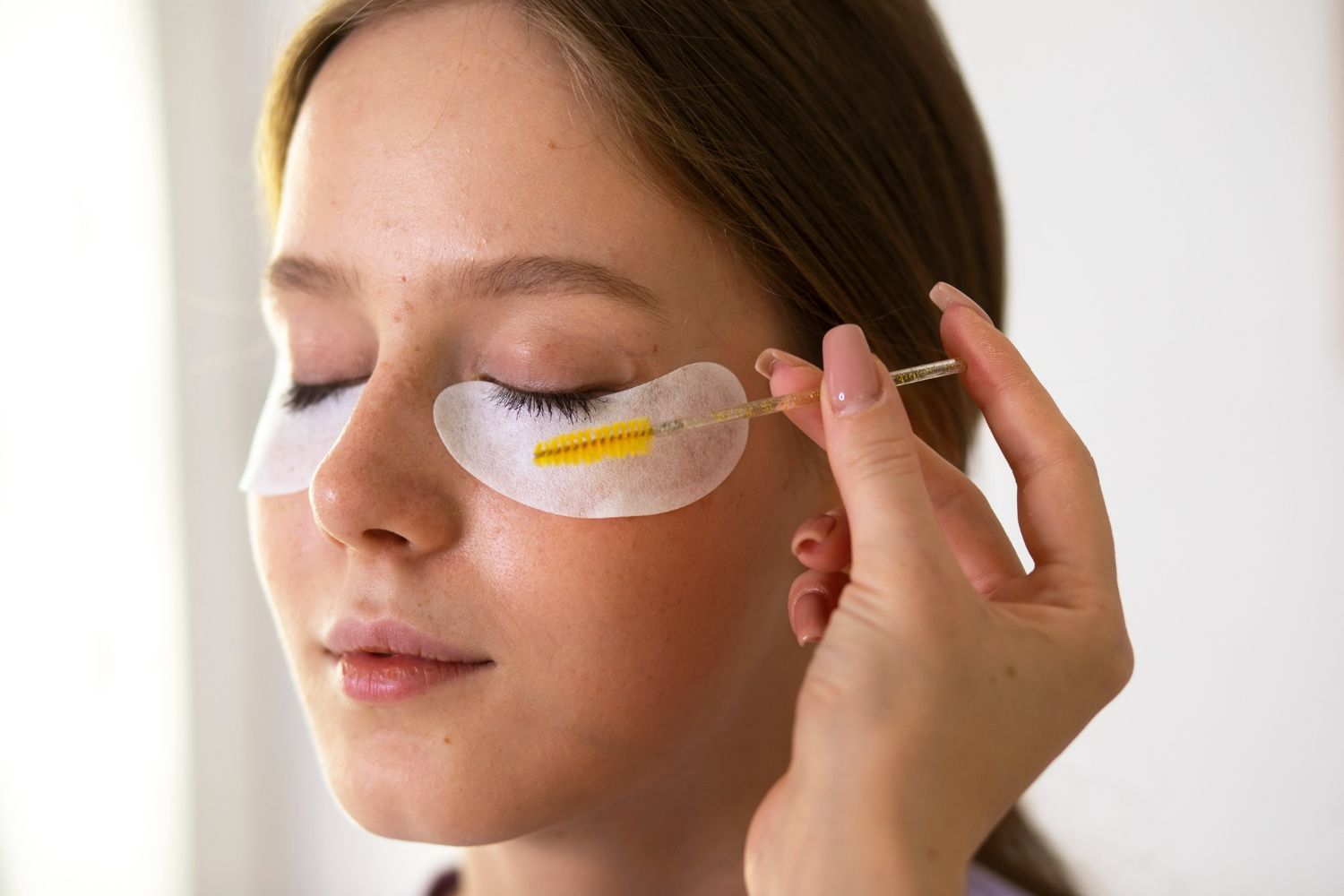 A woman is applying eye patches to her eyes.