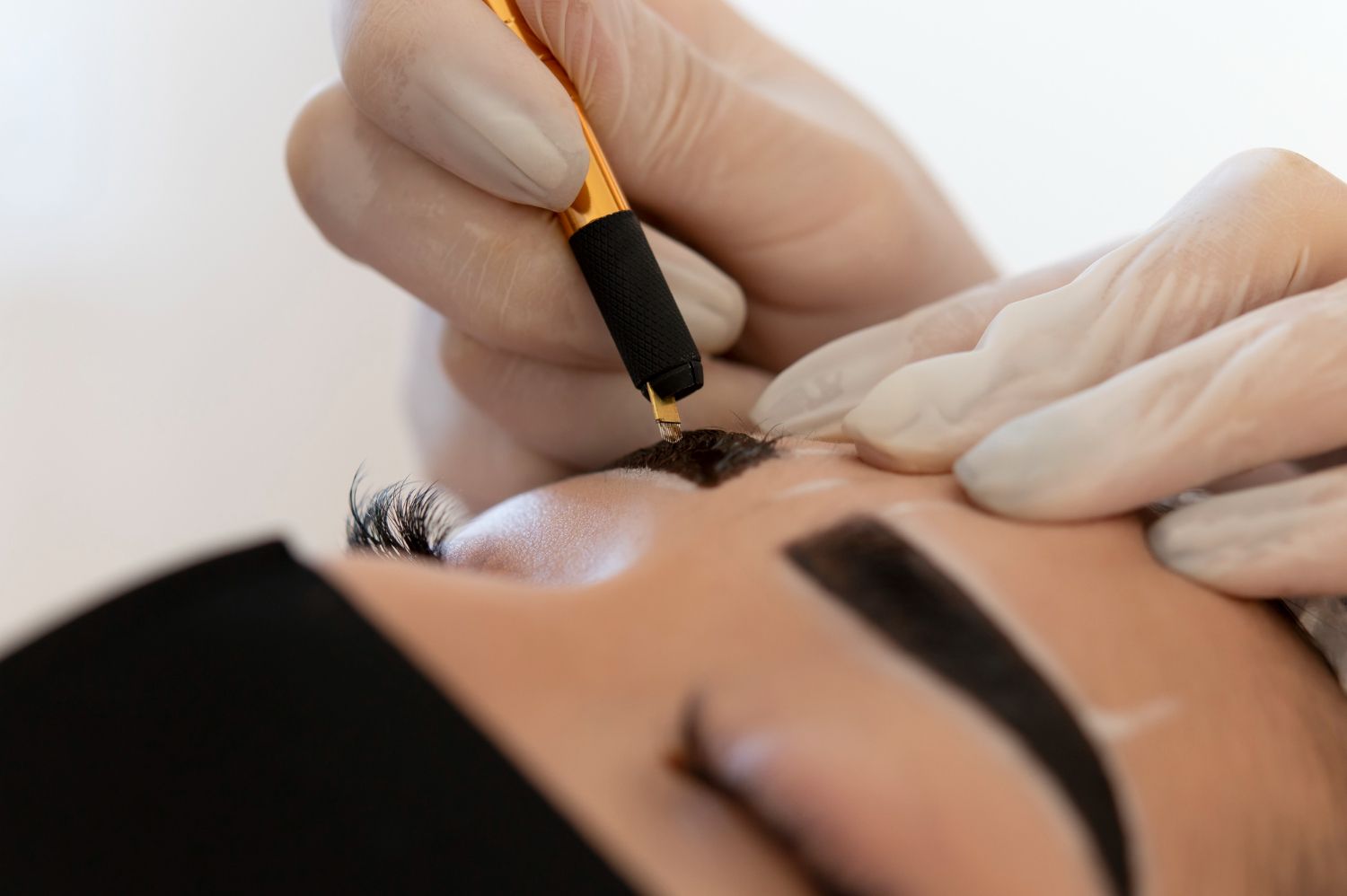 Tattoo artist applying ink with a machine to a client’s eyebrow area