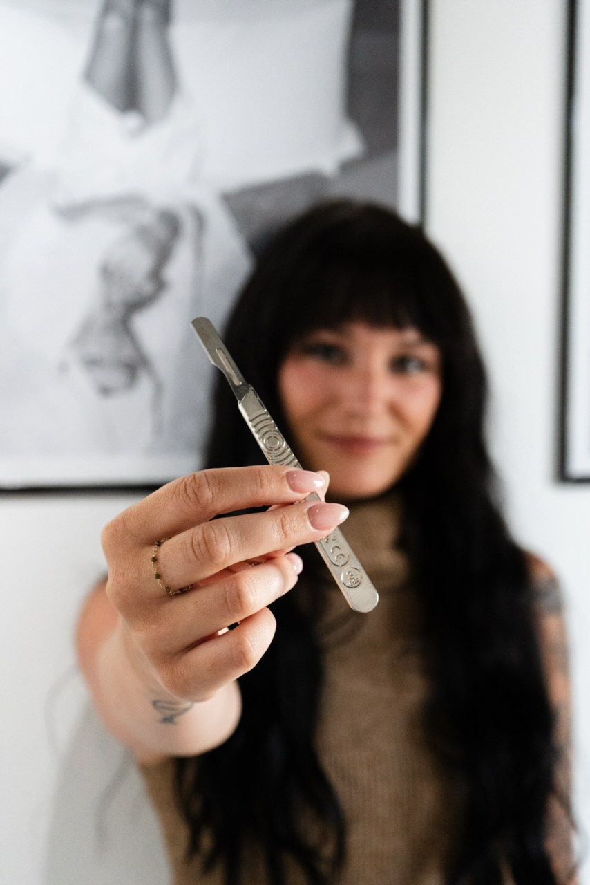 Woman holding tweezers, smiling, in front of framed artwork.