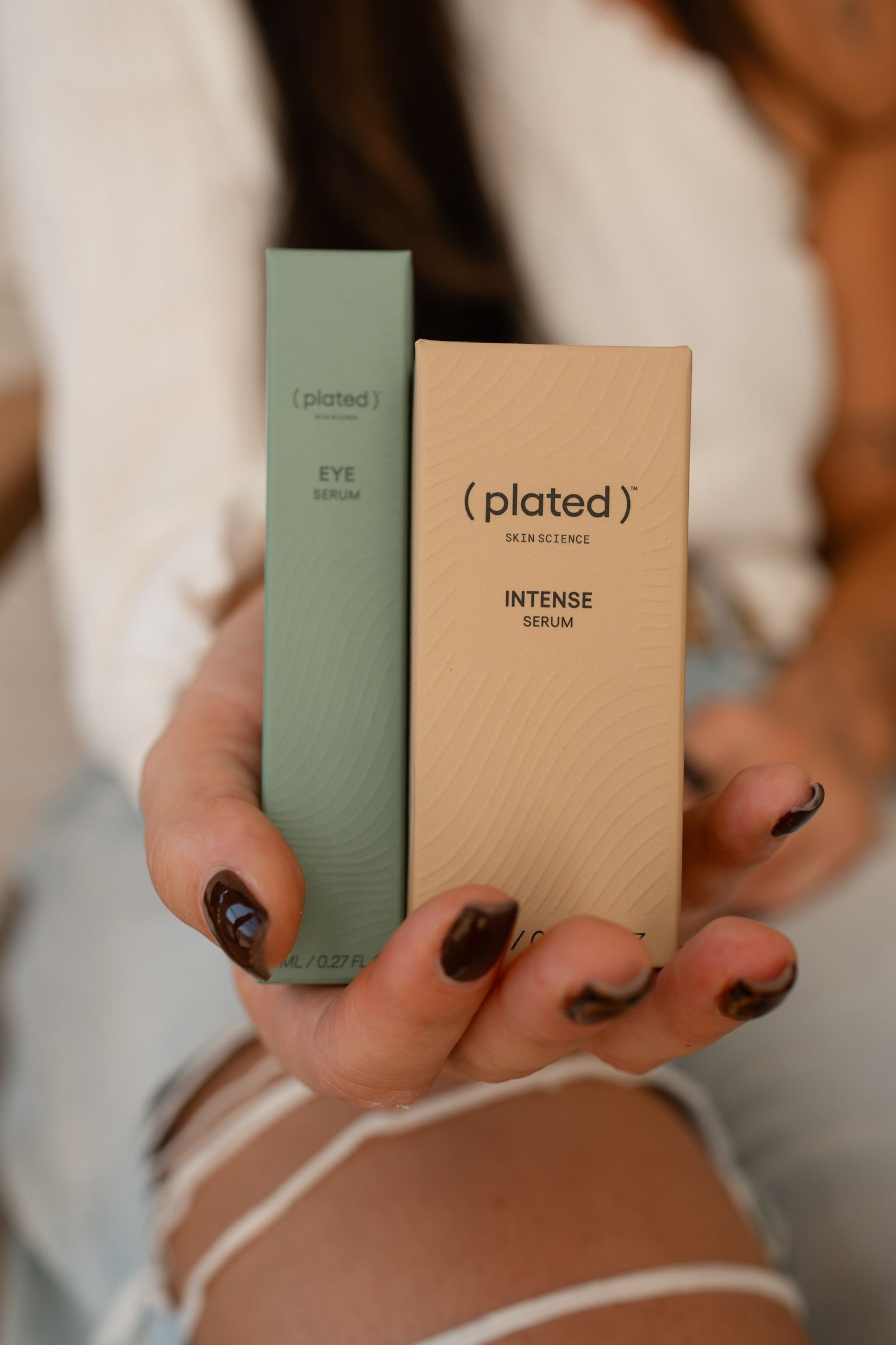 Person holding two rectangular product boxes: green and beige, with minimalist branding.