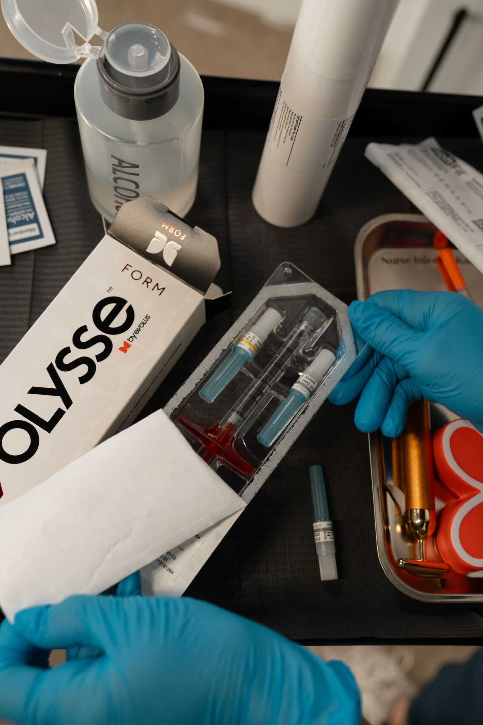Hands in blue gloves holding cosmetic syringes next to a box labeled 