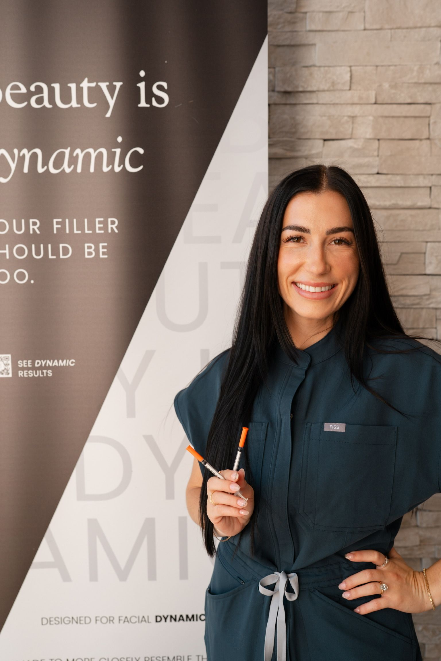 Woman in teal scrubs holds syringes, smiling next to a banner about dynamic beauty.