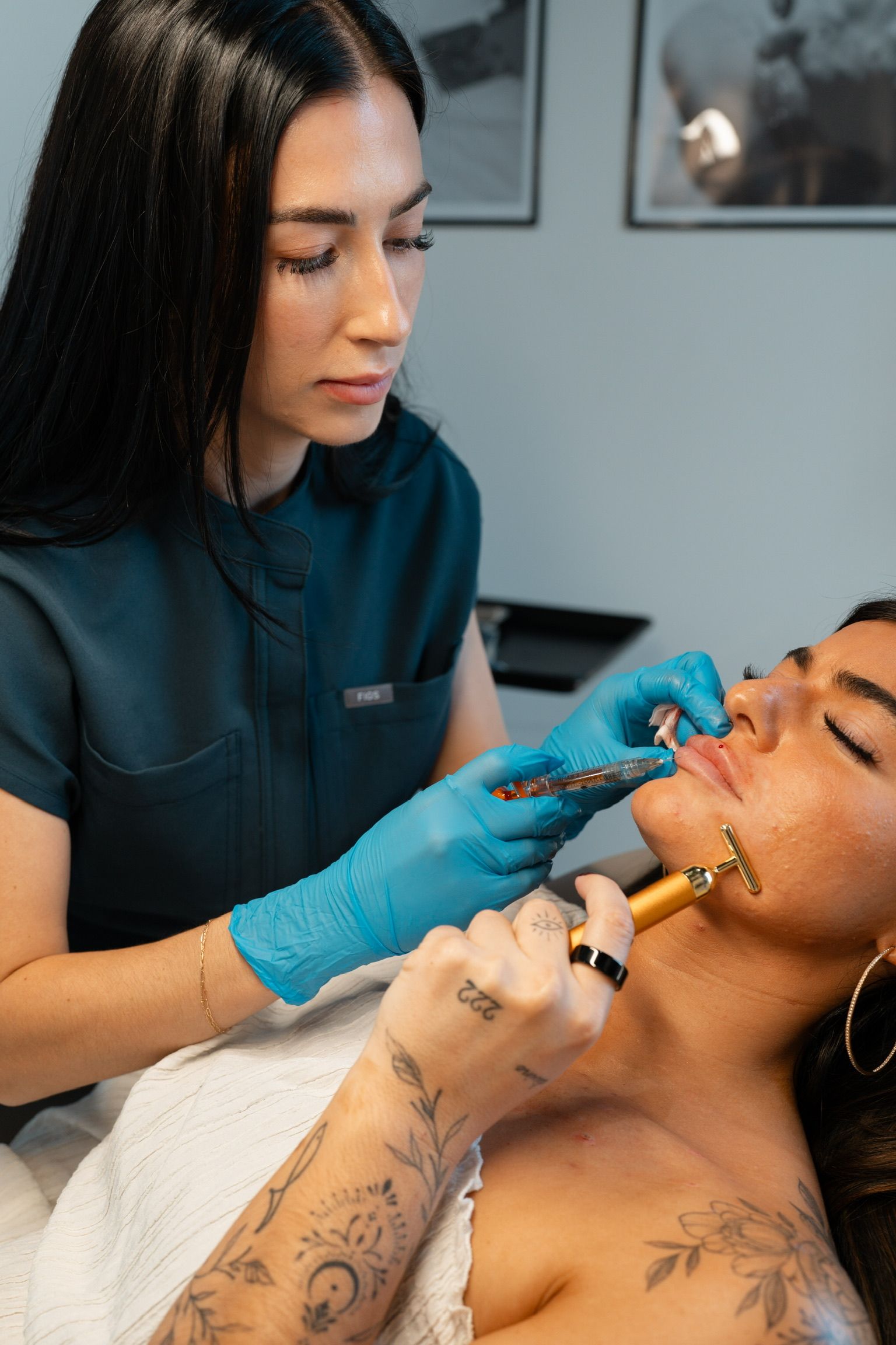 A person receiving a lip injection, with gloved hands and a golden facial tool in place.