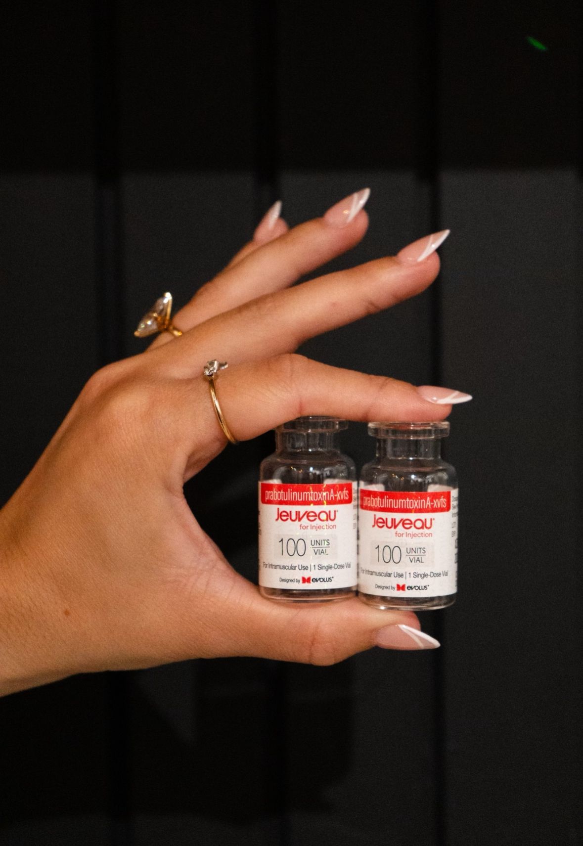 Hand holding two vials with red labels. Clear liquid visible in the vials.