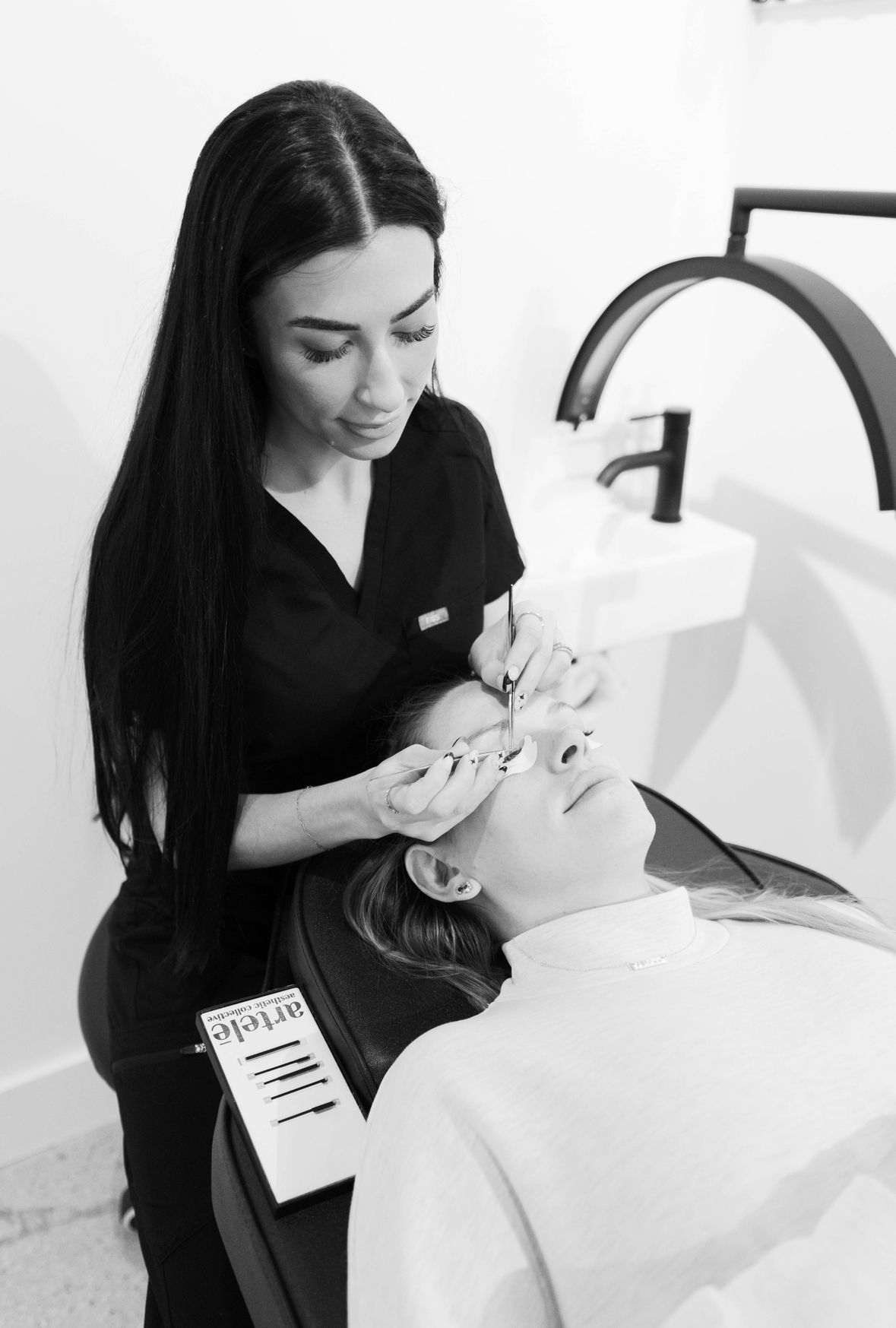 Woman applying eyelash extensions to a client in a beauty studio.