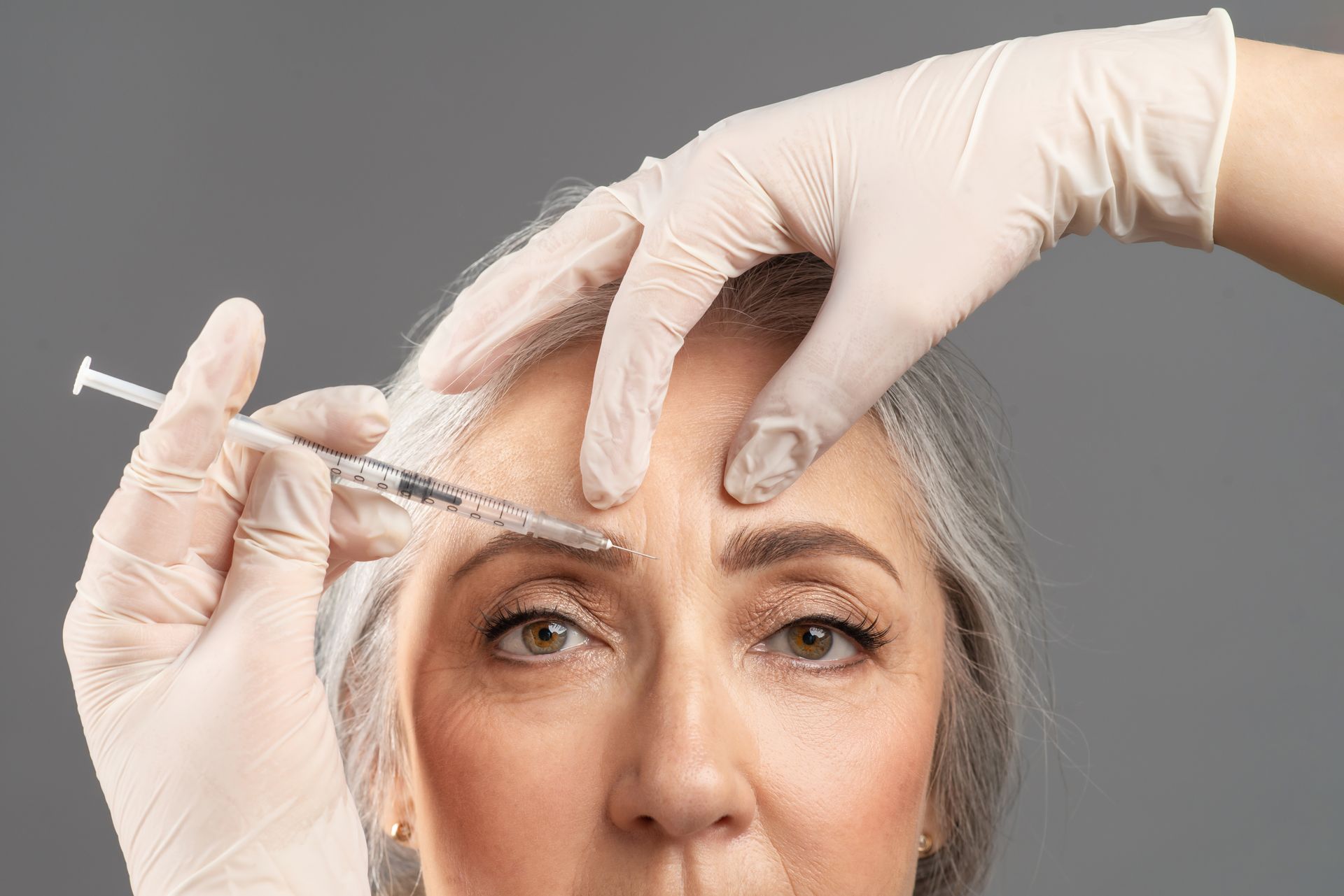A woman is getting a botox injection in her forehead.