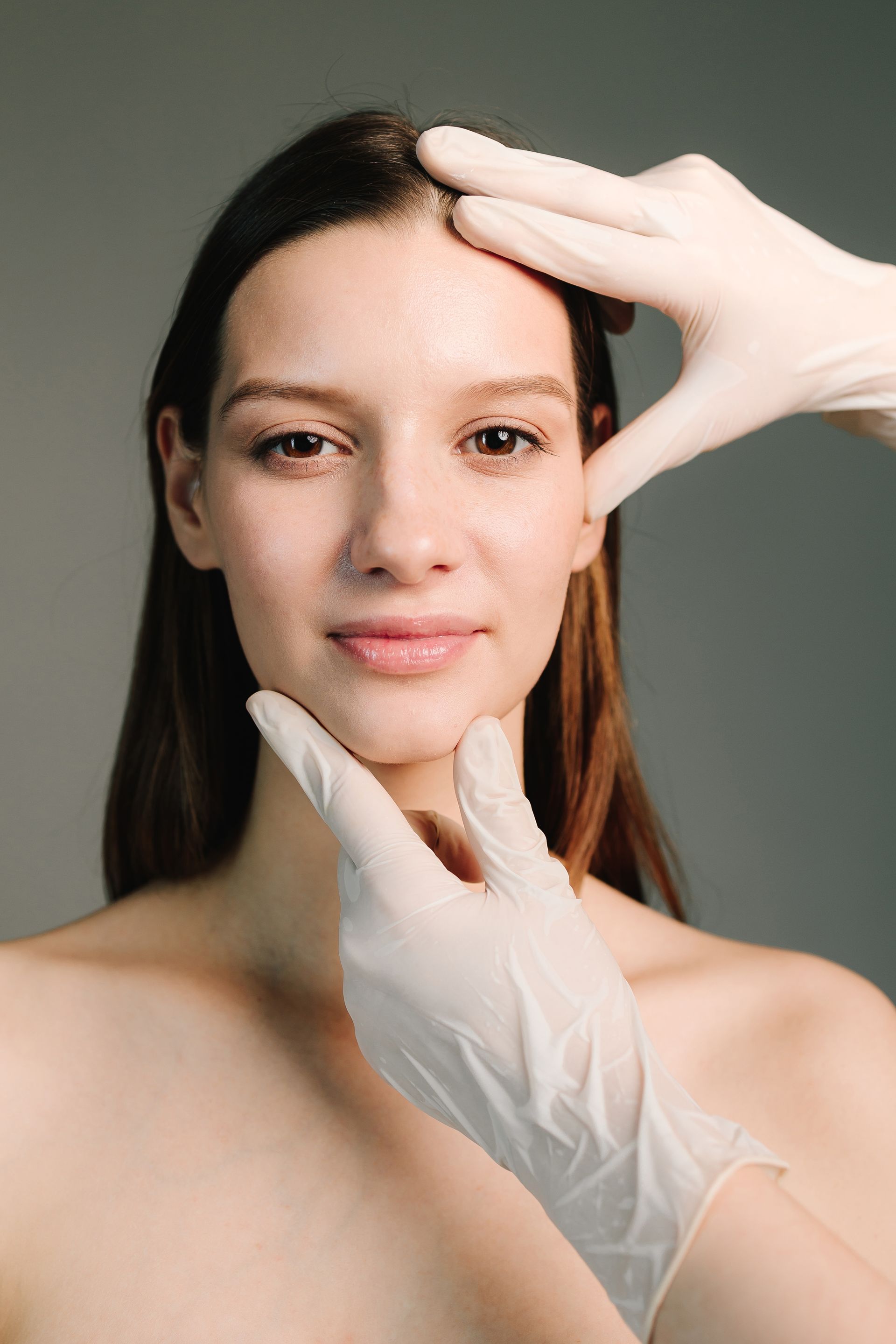 A person's face being examined by hands wearing white medical gloves.