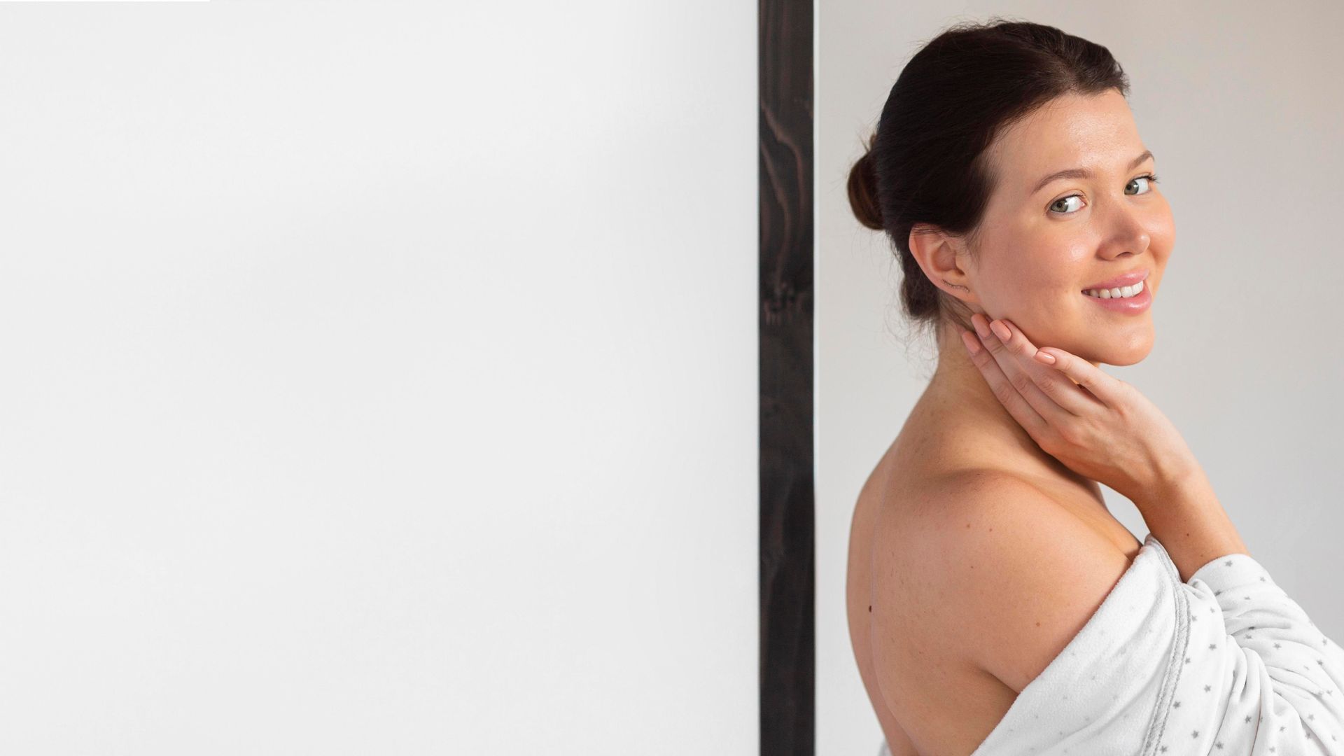 A woman in a white robe is standing in front of a mirror.
