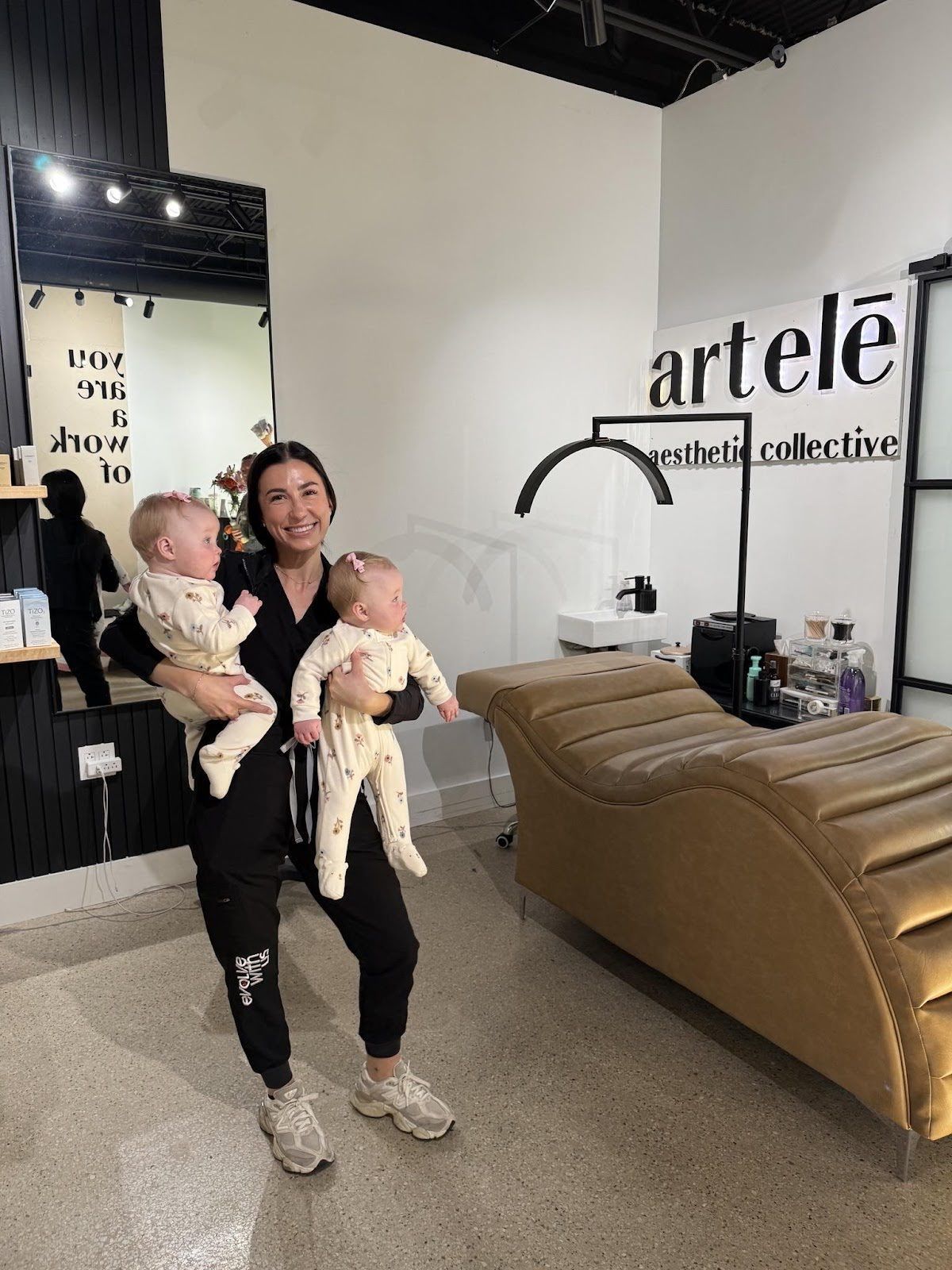 Woman in black scrubs holds two babies in an aesthetic studio.