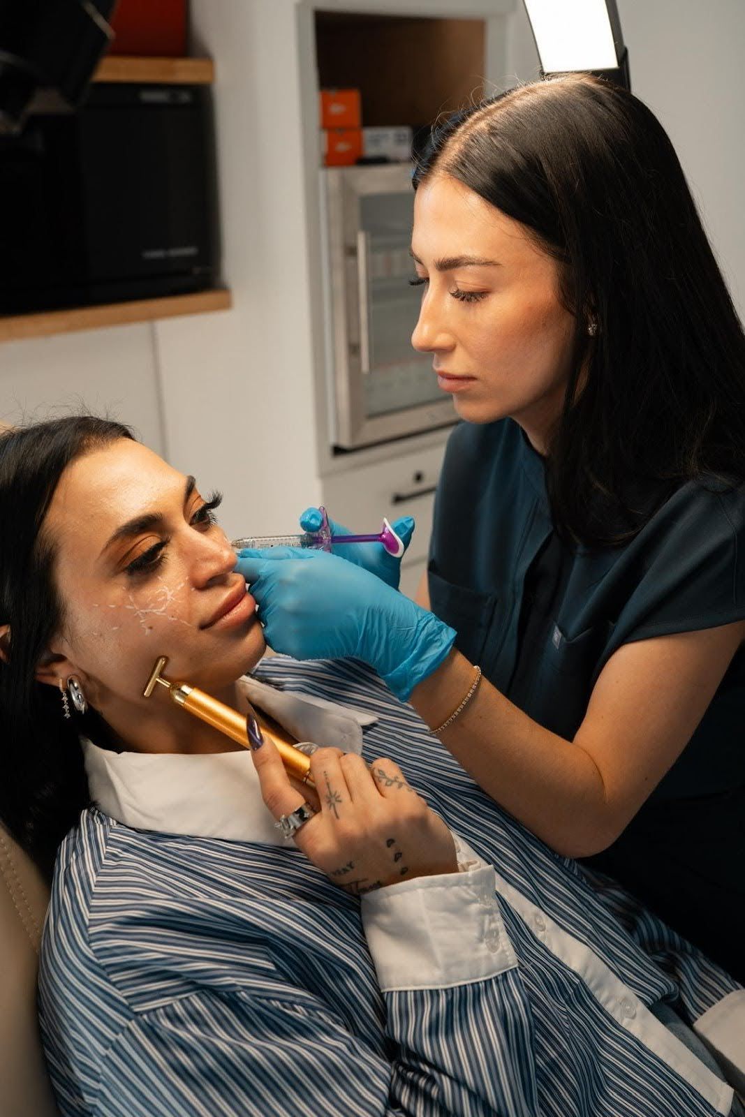 Woman receiving a facial treatment. Aesthetician in blue gloves touches client's face with a device in a medical setting.