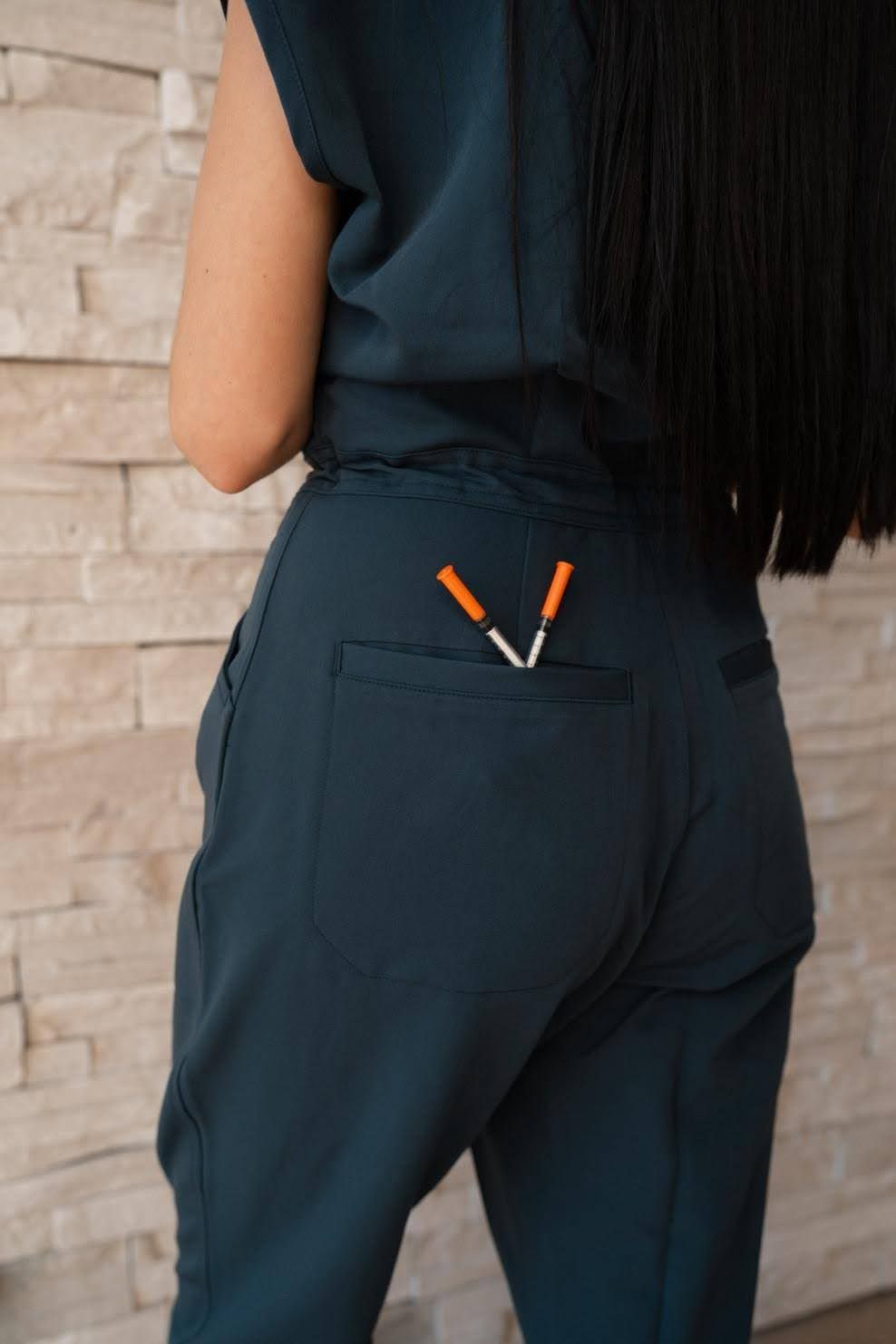 Person wearing teal scrubs with two orange tipped syringes in their back pocket.
