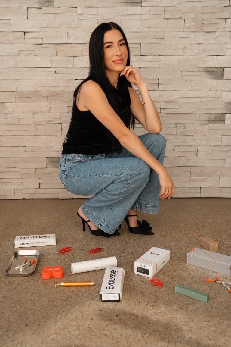 Woman crouching, smiling, surrounded by art supplies, in front of a textured wall.