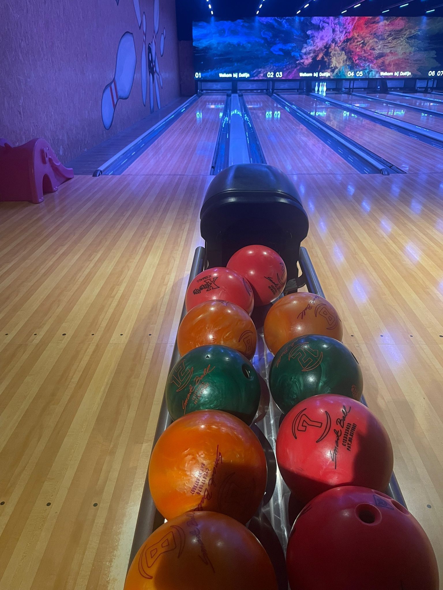 Bowling balls in a rack, on a wooden lane, in a bowling alley, awaiting use.