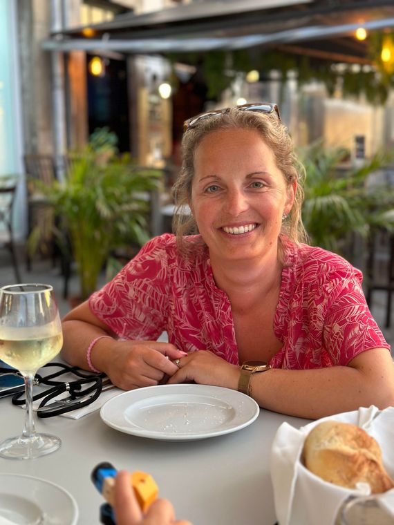 Marit zit aan een tafel met een bord eten en een glas wijn.