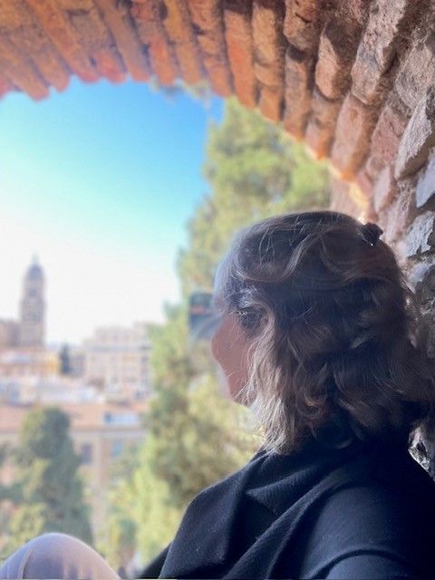 Een vrouw kijkt vanuit een bakstenen boog naar de skyline van een stad onder een helderblauwe hemel.