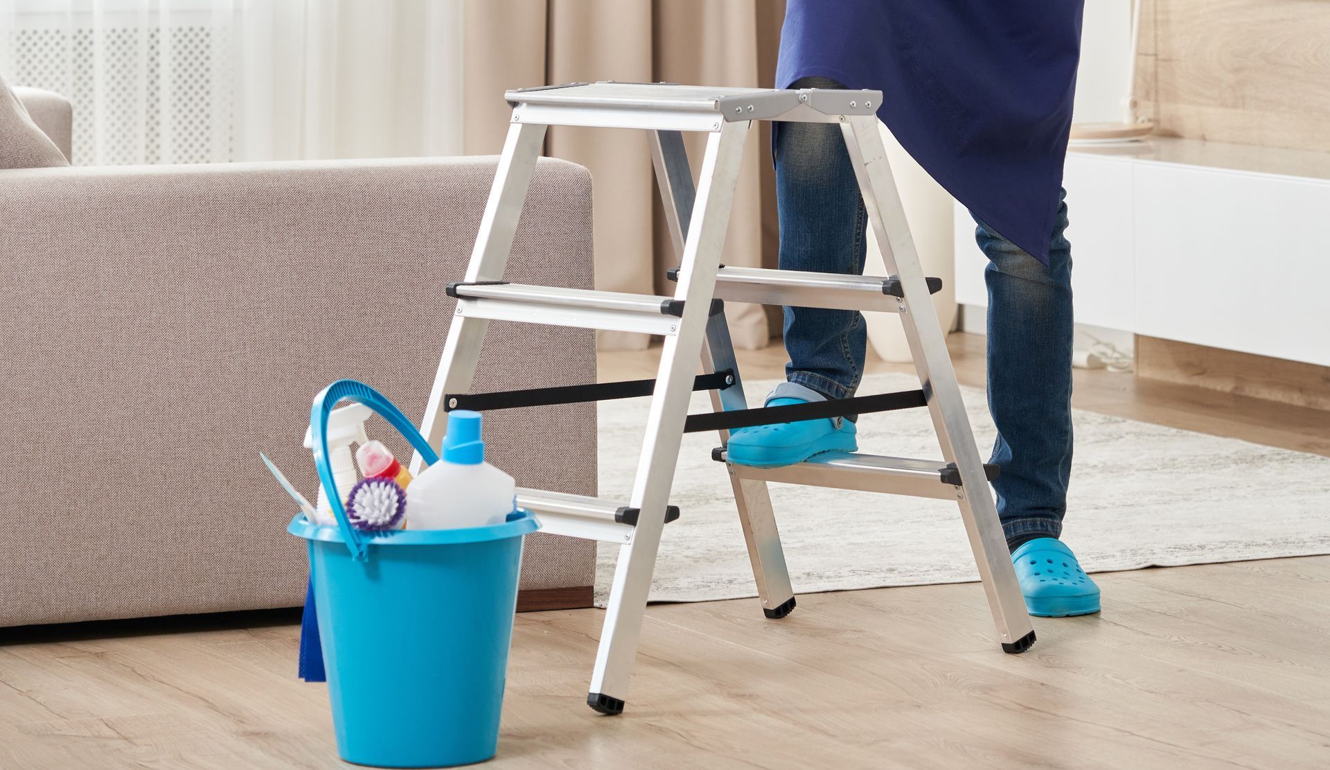 Person on step stool with blue bucket of cleaning supplies. Person on step stool with blue bucket of cleaning supplies.