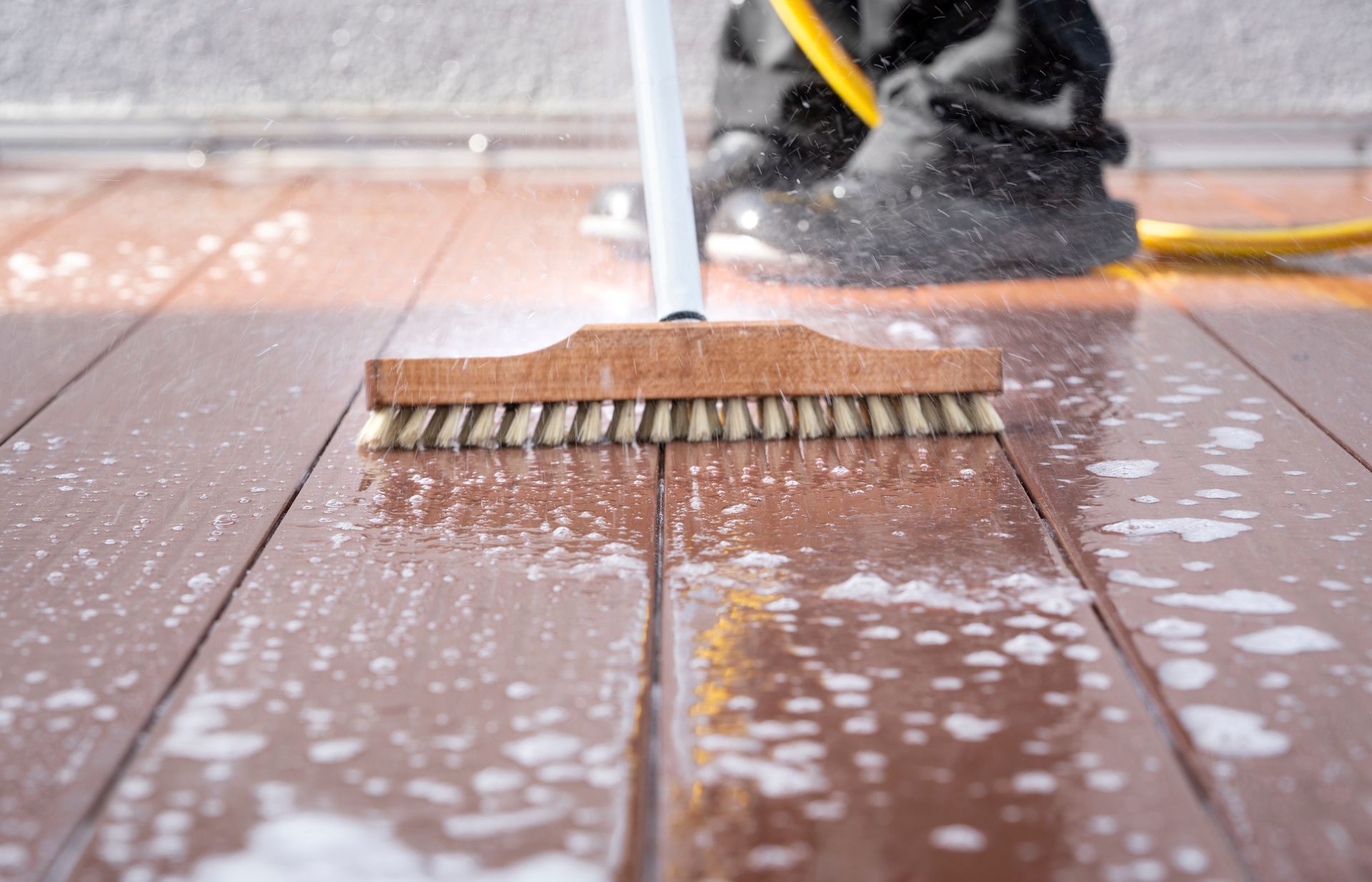 Person scrubbing a wooden deck with a brush and soapy water. Person scrubbing a wooden deck with a brush and soapy water.