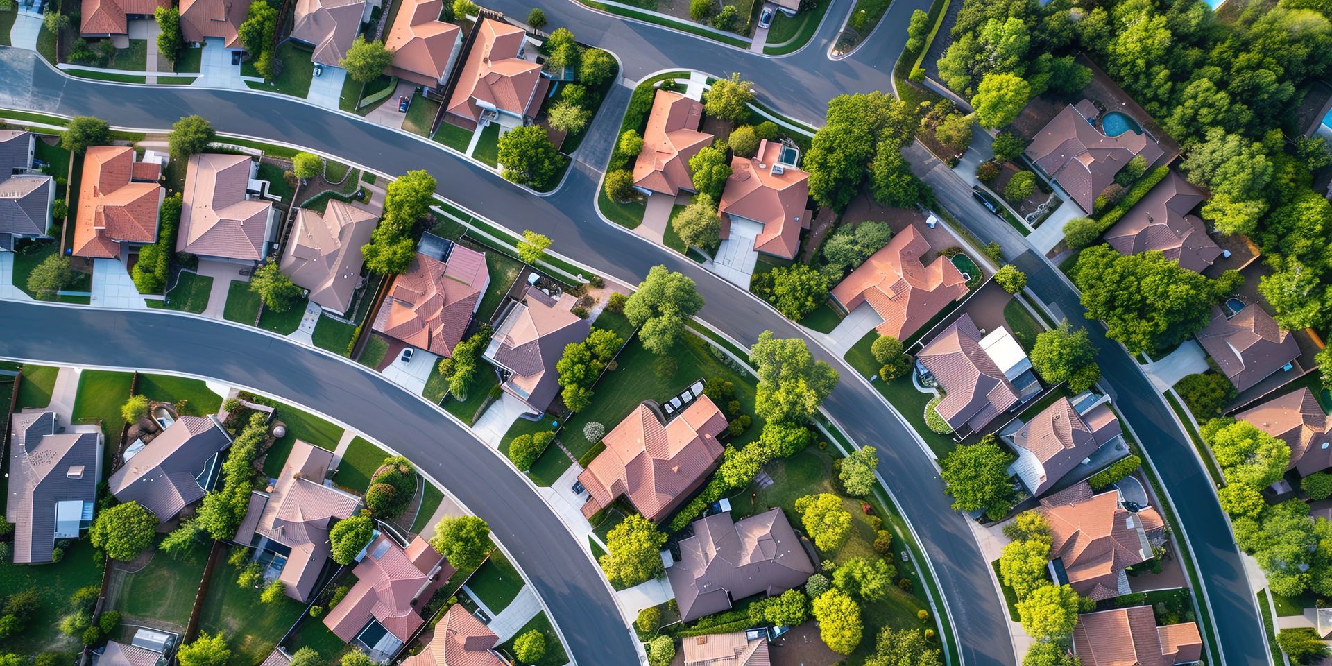 Aerial view of a residential neighborhood with houses, curved roads, and green trees.