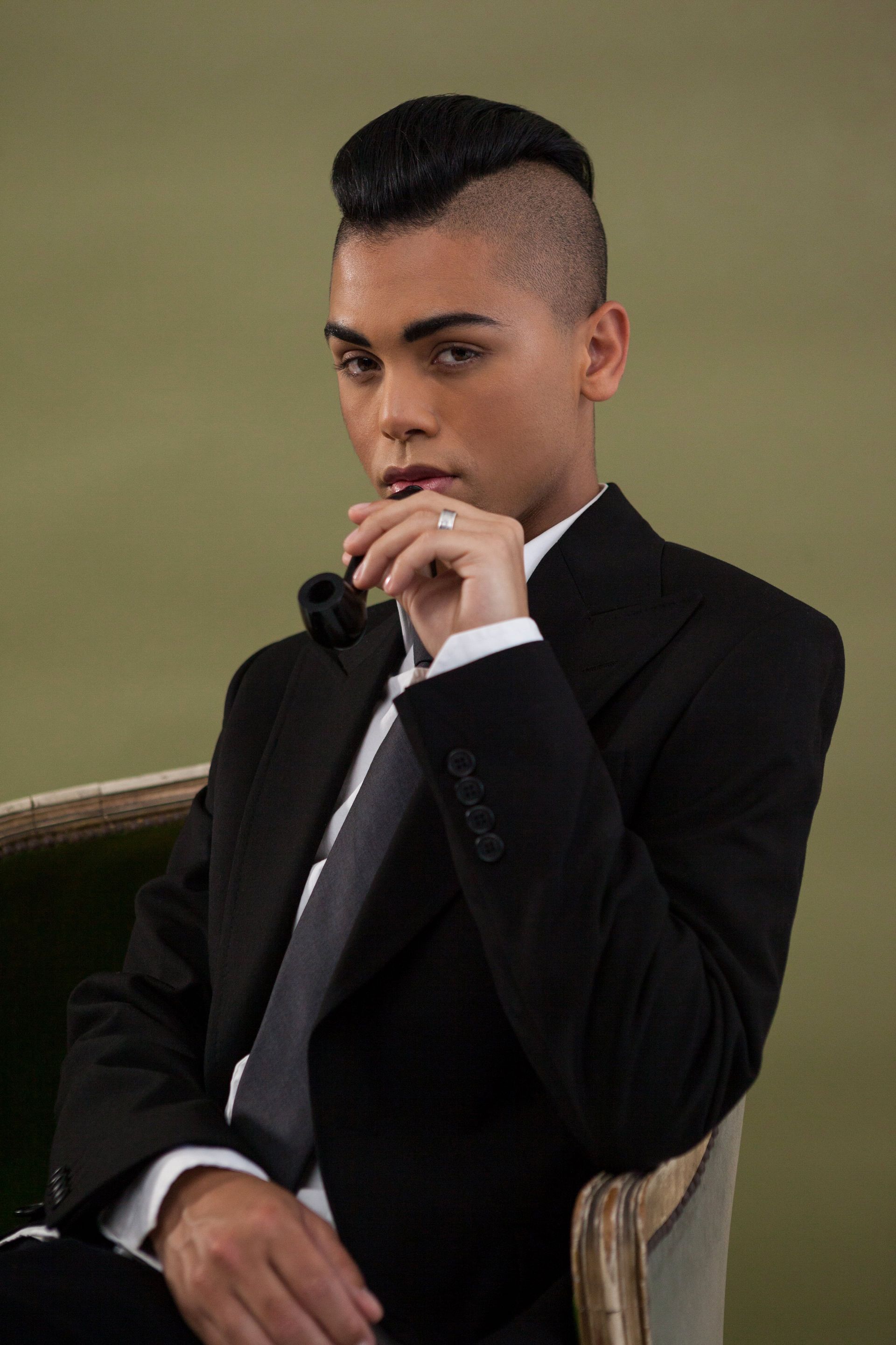 A young person with pink hair is wearing a fur coat and sunglasses.