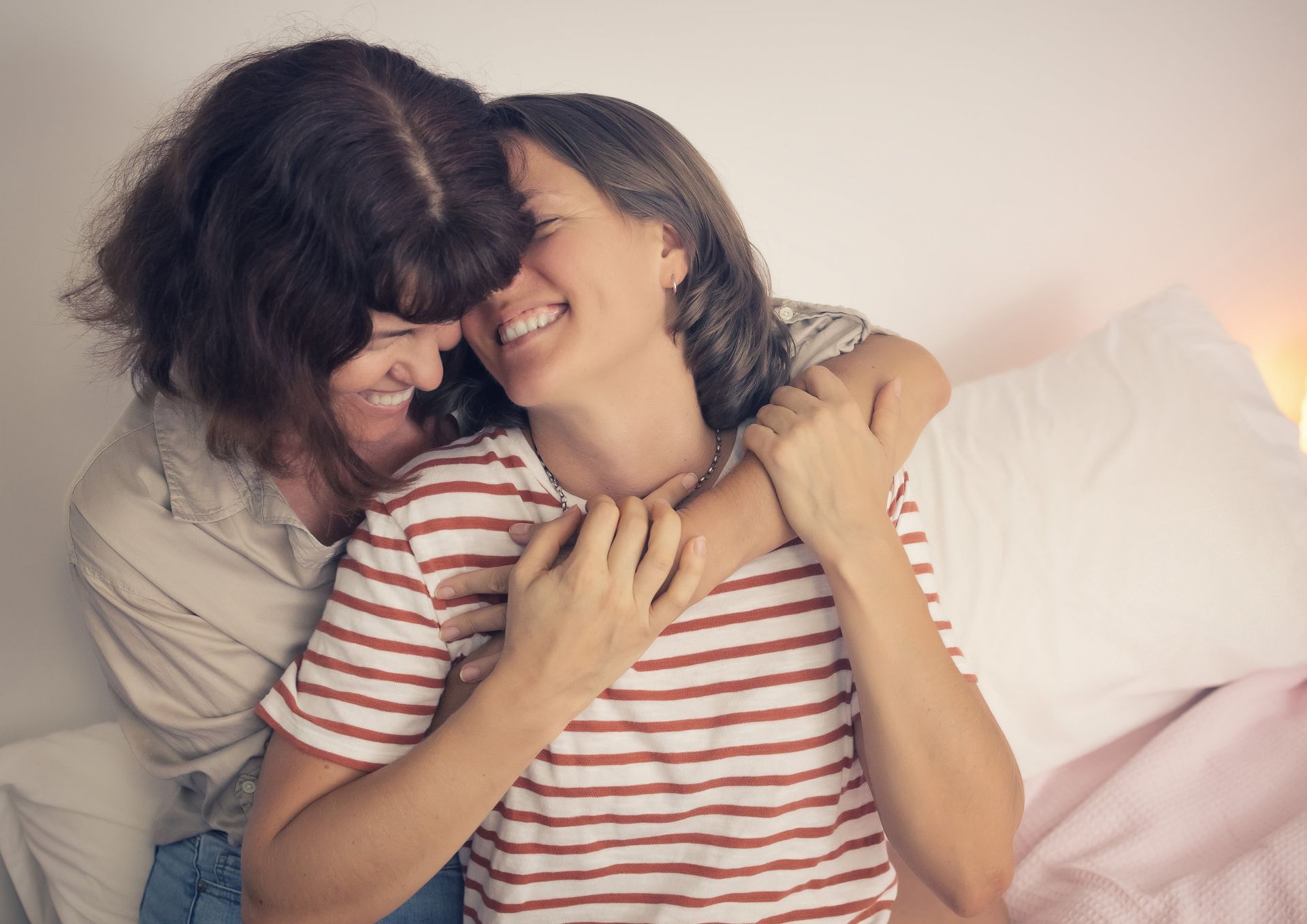 A couple are hugging each other on a bed and smiling.