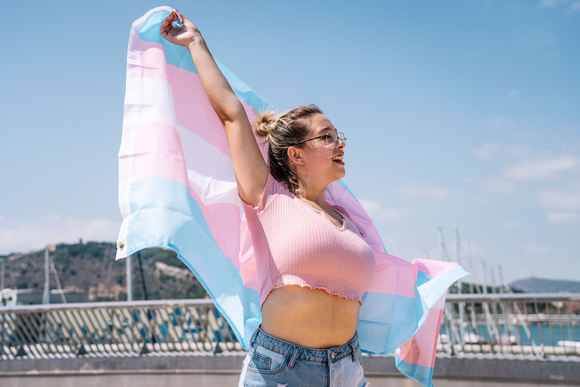 A woman is holding a transgender flag with her arms outstretched.