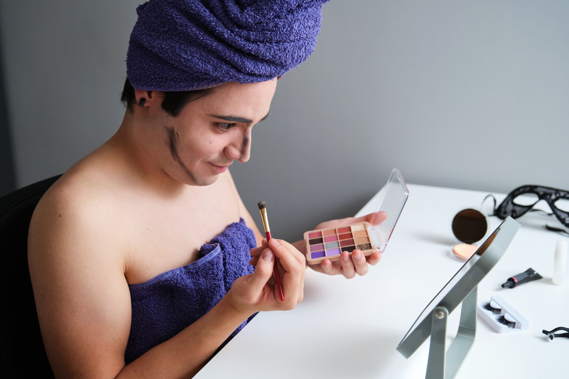 A person with a towel wrapped around their head is applying makeup.