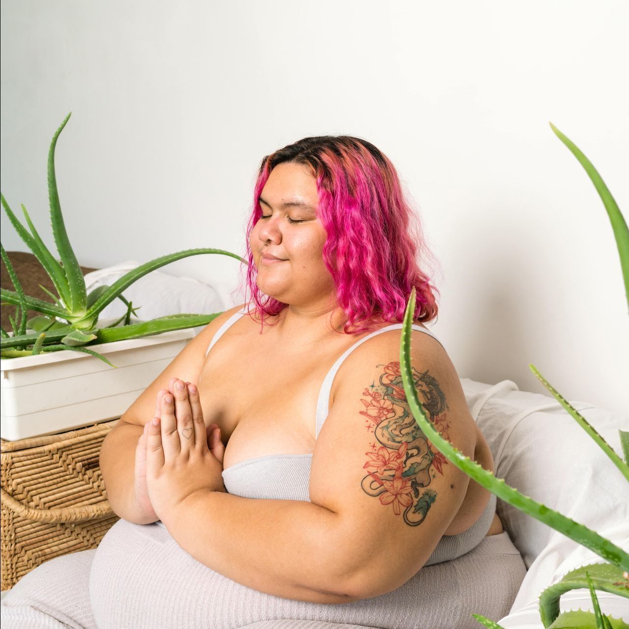A person with pink hair and a tattoo on their arm is meditating