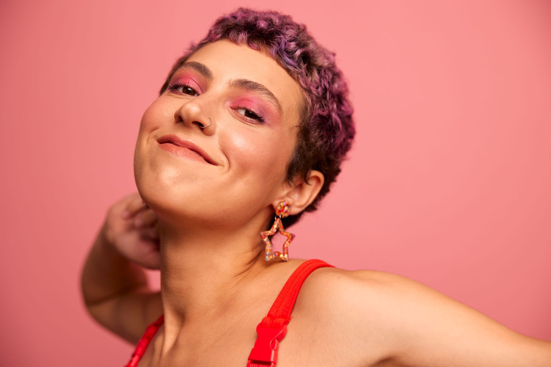 A person with short purple hair is wearing a red shirt and earrings.