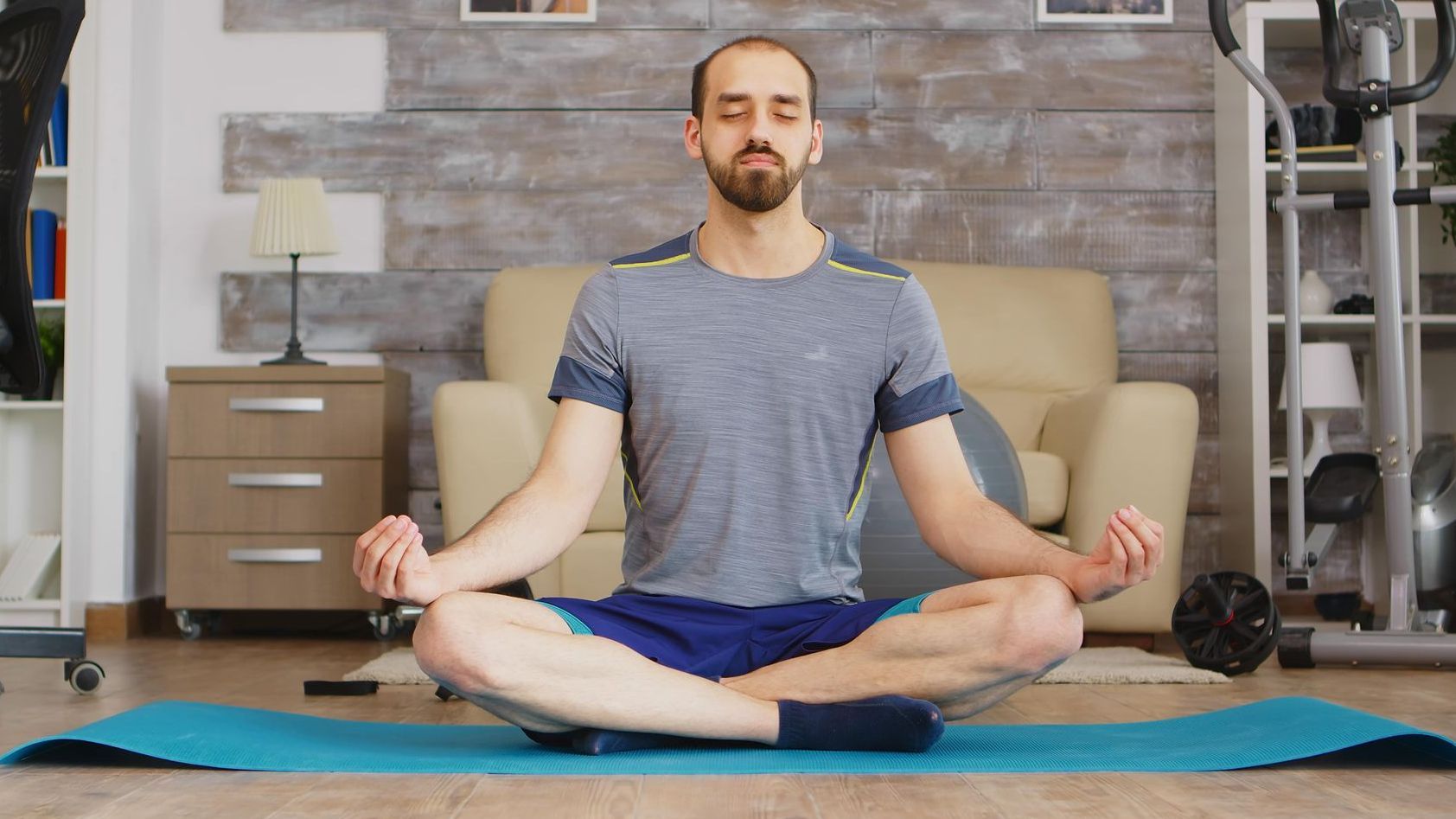 a man is sitting in a lotus position on a yoga mat in a living room .