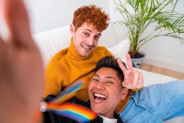 Two men are sitting on a couch making a peace sign.