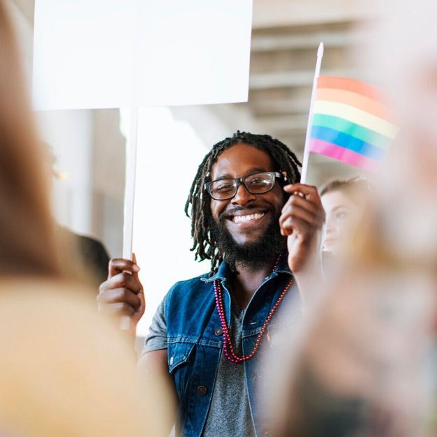 A person is holding a sign and a rainbow flag.