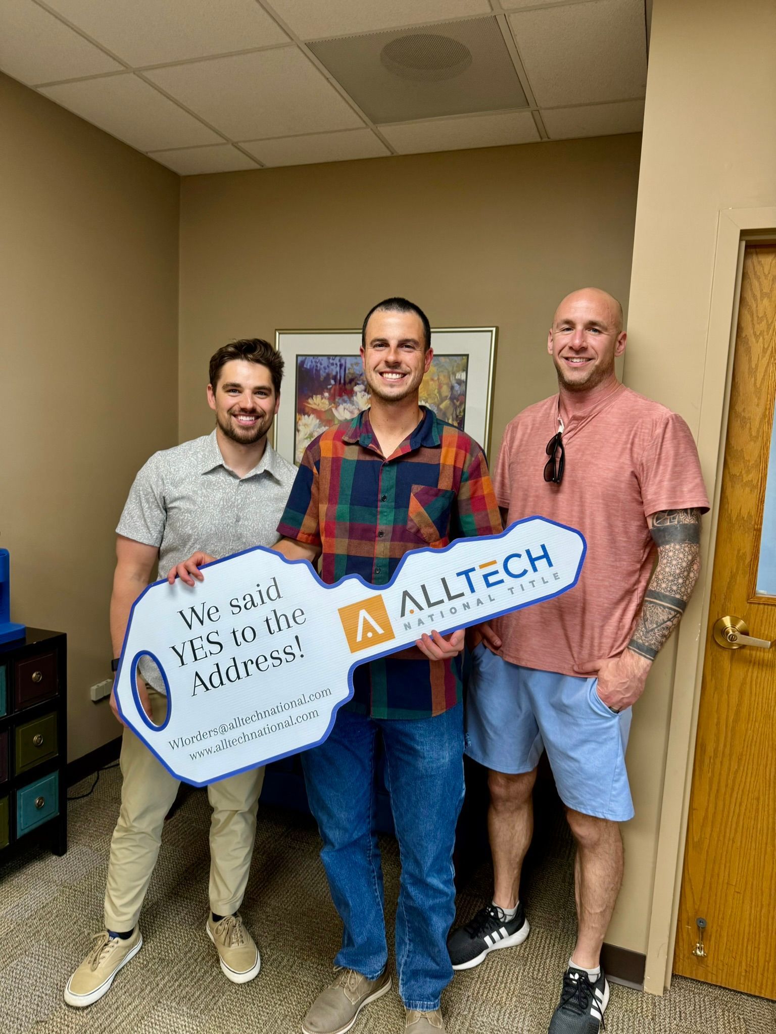 Three men in an office holding a large key. One man smiles, holding the key, others look on.