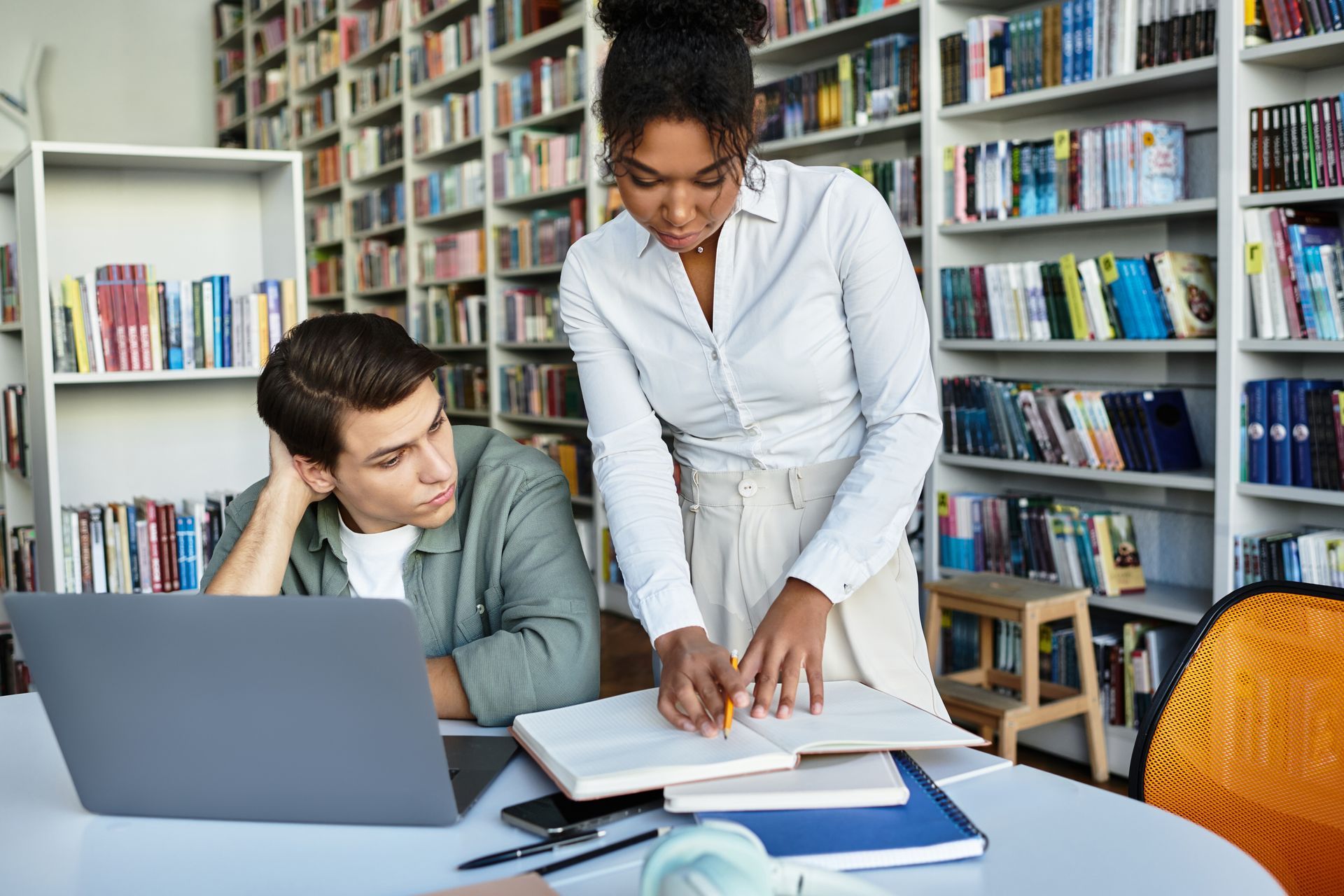A woman is helping a man with his homework in a library.